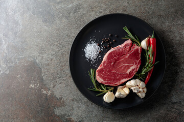 Raw beef steak with rosemary, garlic, salt, and pepper.