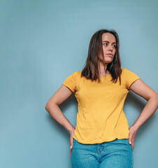 Portrait of a woman in a yellow T-shirt against a blue background, hands at the sides - obrazy, fototapety, plakaty