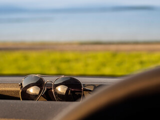 Dark dirty sun glasses on dash board. Beautiful nature scene with ocean and mountains in the background. Travel and trip by car to nature concept.