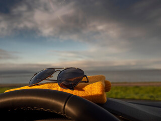 Yellow hat on dash board behind steering wheel and dark dirty sun glasses. Beautiful nature scene with ocean and mountains in the background. Travel and trip to nature concept.