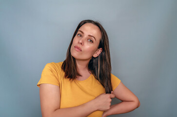 Obraz premium Woman is holding lock of black hair. Yellow T-shirt, Blue Background