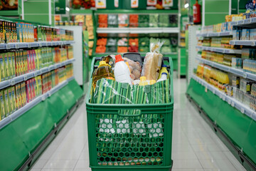 Shopping Cart Full of Groceries in the Supermarket, Vegetables on Background - Consumerism Concept,...