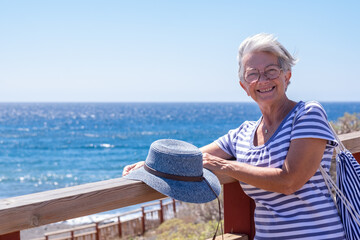 Fototapeta na wymiar Happy cheerful senior woman in outdoors summer sea. White haired smiling lady dressed in blue expressing freedom and joy. Horizon over water