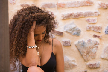 beautiful brunette woman with curly hair on a stone background is sad and dazed with a lost look of pain and despair. The woman is dressed in black because of the pain of the loss of a family member