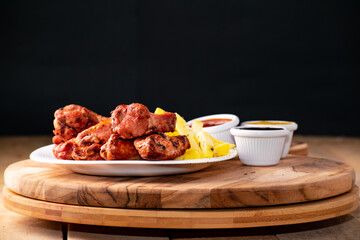 bbq chicken wings with french fries and ketchup, mustard and bbq on a rustic wooden table on a black background