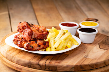 bbq chicken wings with french fries and ketchup, mustard and bbq on a rustic wooden table on a black background