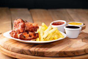 bbq chicken wings with french fries and ketchup, mustard and bbq on a rustic wooden table on a black background