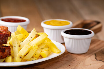 bbq chicken wings with french fries and ketchup, mustard and bbq on a rustic wooden table on a black background