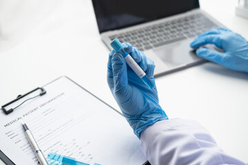 Doctor holds test tube and using on laptop. entering test results into the database.