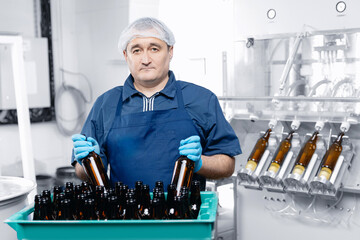 Worker checks and prepares glass brown bottles in plastic box are designed for beer bottling....