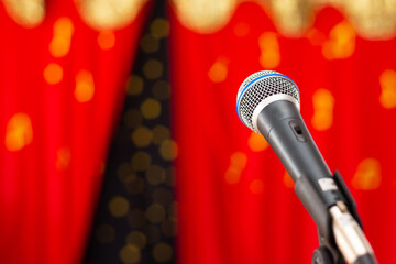 Um microfone preto, em um palco com cortina vermelha desfocada ao fundo.