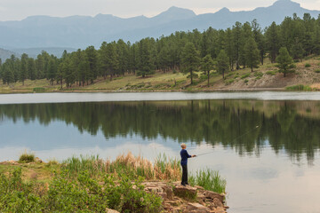 Obraz premium A young male is fishing on a beautiful mountain lake in Colorado in the United States.