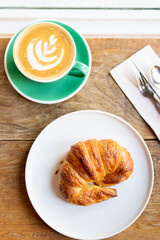 Cup of coffee with latte art with croissants on wooden table and morning sunlight with shadow through from window. Beautiful meal with warm sunlight.