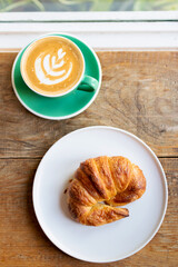 Cup of coffee with latte art with croissants on wooden table and morning sunlight with shadow through from window. Beautiful meal with warm sunlight.