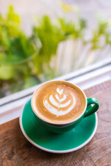 Cup of coffee with latte art on wooden table and morning sunlight with shadow through from window. Beautiful morning.