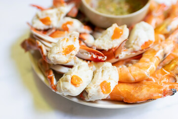 Steamed blue crab legs and shrimp on plate serving with spicy sauce.