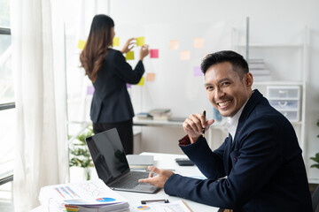 Professional businessman working with laptop computer with his coworker in the background.