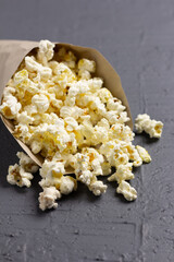 Eco-friendly paper cone filled with popcorn spilled on textured surface.