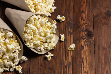 Eco-friendly paper cones filled with popcorn spilled on wooden surface.