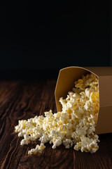 Eco-friendly paper bowl filled with popcorn that is scattered over a wooden surface.