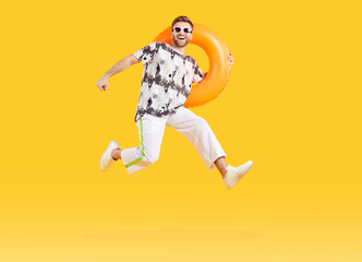 Full body photo of a young man in sunglasses holding rubber ring and jumping isolated on studio...