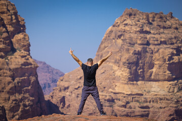 Petra w Jordanii. Mężczyzna stojący na szczycie skalnej góry na tle błękitnego, niebieskiego...