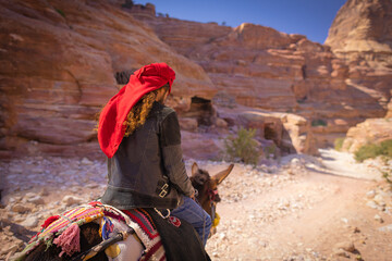 Petra w Jordanii. Człowiek jadący na ośle pomiędzy pustynnymi skałami. - obrazy, fototapety, plakaty
