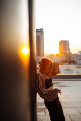 Stylish woman enjoys incredible view of the city from the rooftop at sunset. Young woman posing on the rooftop.Style, fashion or freedom concept, lifestyle.