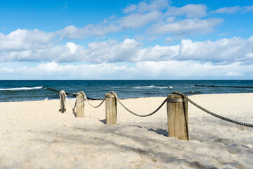 Wooden bollards on a sunny beach on the Baltic Sea, a thick rope connects the wooden beams
