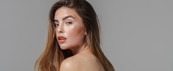Studio beauty portrait of very natural woman with freckles on her face and shoulder. Girl looking...