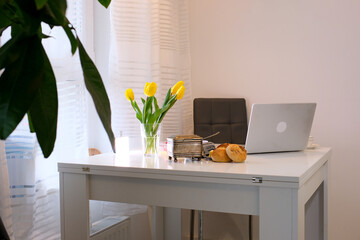 Dining table with setting and vase served for International Women's Day celebration in modern kitchen. laptop yellow tulips for breakfast buns High quality photo