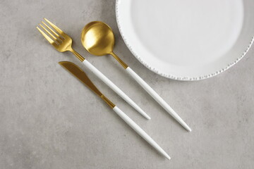 Empty white plate and cutlery on a gray  stone table top view with space for text .Modern minimal...