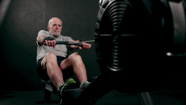 An old elderly man in sportswear is training in the gym doing weight lifting with dumbbells. Leisure healthy lifestyle. An elderly man is exercising. Fitness for the elderly. active pensioners.