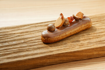 Eclair with hazelnuts in chocolate glaze on a wooden board
