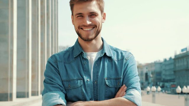 Portrait of handsome smiling stylish hipster lumbersexual model. Man dressed in jeans jacket clothes. Fashion male posing on the street background