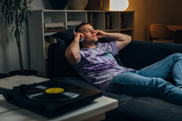 Fototapeta premium A Caucasian man puts on headphones to listen to records and relax at night