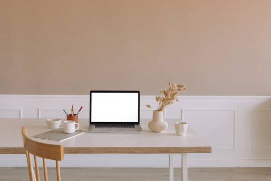 Close-up of an open laptop computer on a table next to dried flowers in a vase, a cup and books