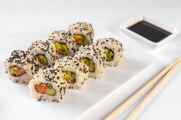 Sushi roll California with salmon, sesame seeds, avocado, cream cheese on white background. Sushi menu, rolls served on white dish and soy sauce. Traditional Japanese cuisine food.