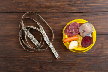 Pet care and diet concept. Bowl of raw food with meat, fish and vegetables on wooden background.