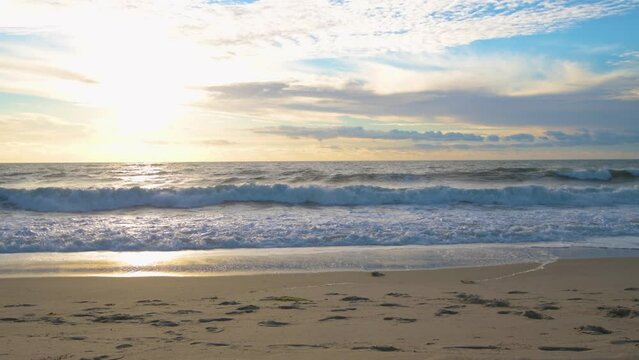 Low-angle shot of sea waves flooding the sandy sunlit Bethany beach at sunset skyline background