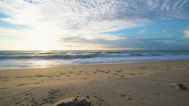 Low-angle shot of sea waves flooding the sandy sunlit Bethany beach at sunset skyline background