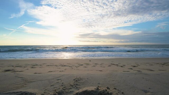 Low-angle shot of sea waves flooding the sandy sunlit Bethany beach at sunset skyline background
