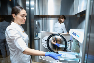 Young woman is sterilizing medical instruments in an autoclave