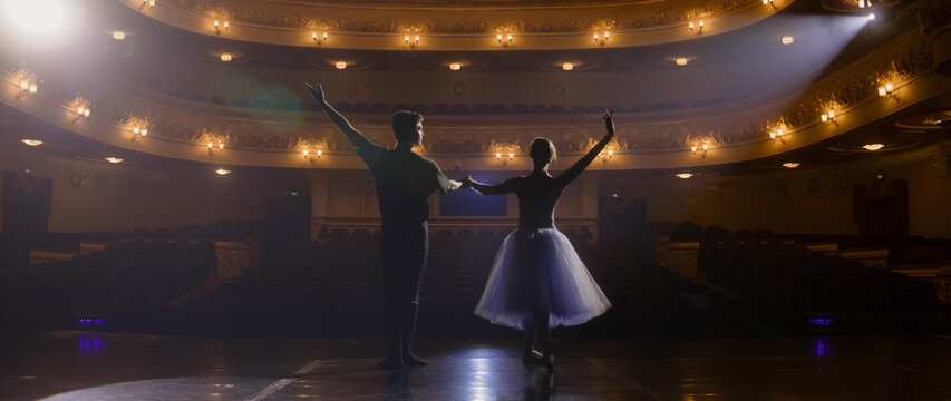 Ballet dancers bow at the end of choreography rehearsal on classic theater stage illuminated by spotlight. Dance partners prepare for theatrical dance performance. Art of classical ballet dance.