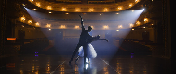 Couple of classical ballet dancers practice on theatre stage before performance. Man in training...