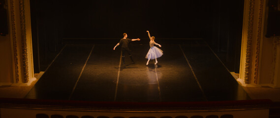 Wide shot of ballet dancers practicing choreography on classic theater stage. Man and woman prepare...