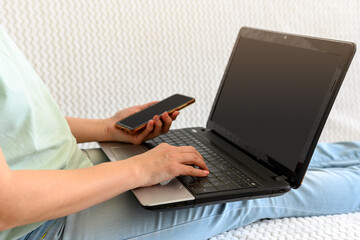 Naklejka premium A girl with a phone in her hands is engaged at home on a laptop with a mug on the couch.