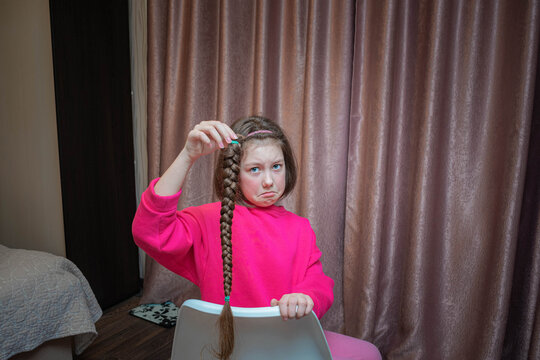A sad girl sitting in a chair holds her long braid in her hands. The child cut his hair.