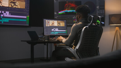 African American colorist makes color grading in video editing software. Multiple monitors with...