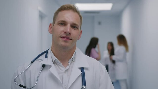 Portrait of a male doctor who looks into the camera against the background of communicating colleagues in the corridor of the hospital